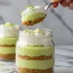 A spoon digging into a Key Lime Pie Jar showing the layers of graham cracker crust